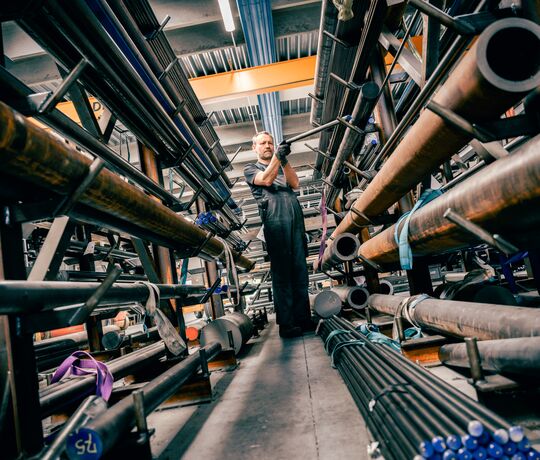 Merarbejder på lager står med et metal emne og er ved at lægge det på plads.